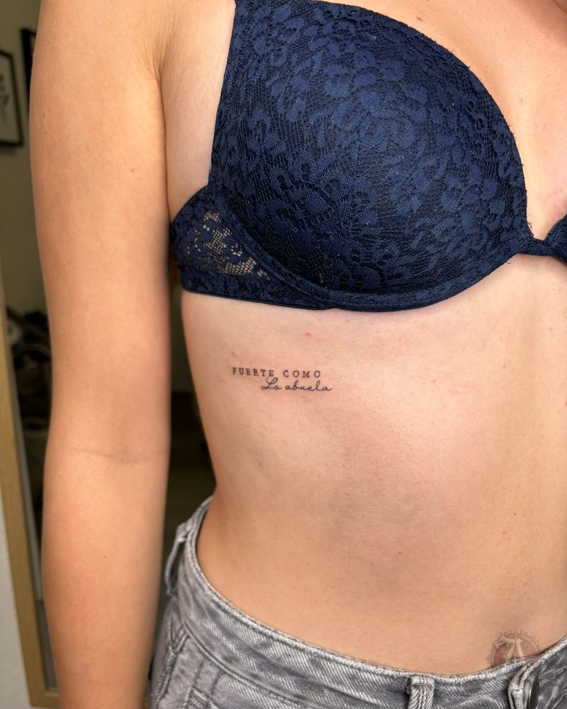 Tatuaje de frase bajo el pecho en el costado, fine line en negro y gris