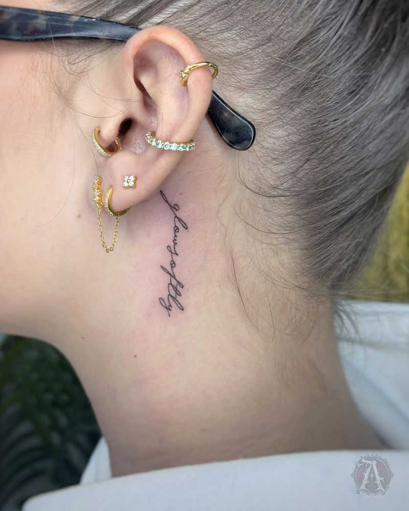 Tatuaje de lettering vertical en detrás de la oreja, fine line en negro y gris